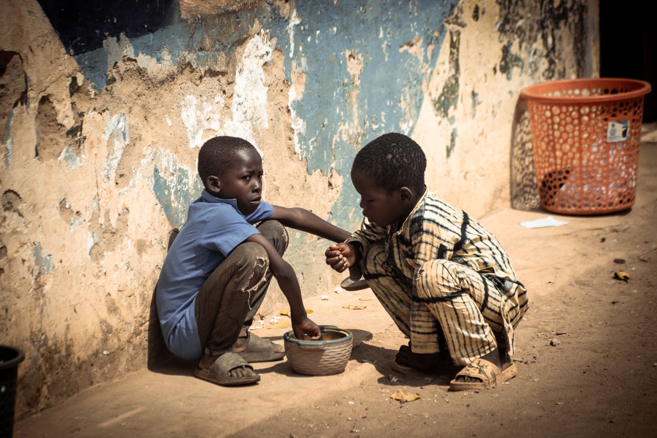 gallery-01 Two boys share a meal outdoors, highlighting themes of poverty and resilience.
