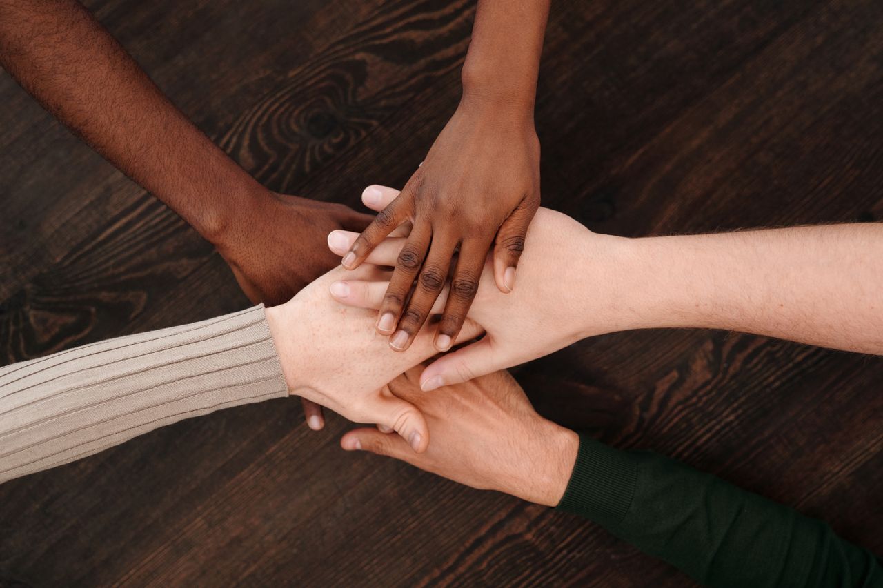 portfolio-06 A diverse group of hands joining together, symbolizing unity and teamwork on a wooden surface.