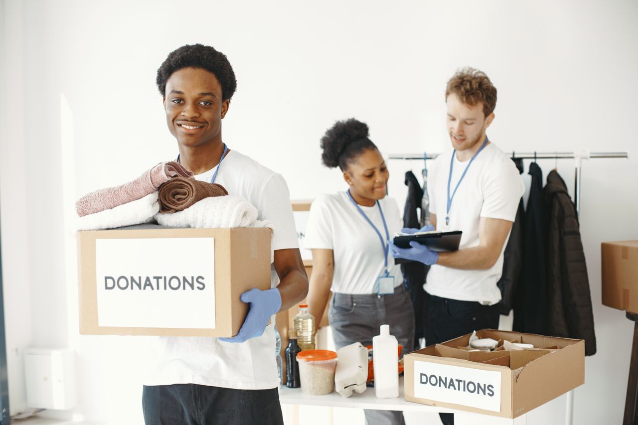 services-01 Diverse group of volunteers organizing donation boxes with clothes and supplies indoors.