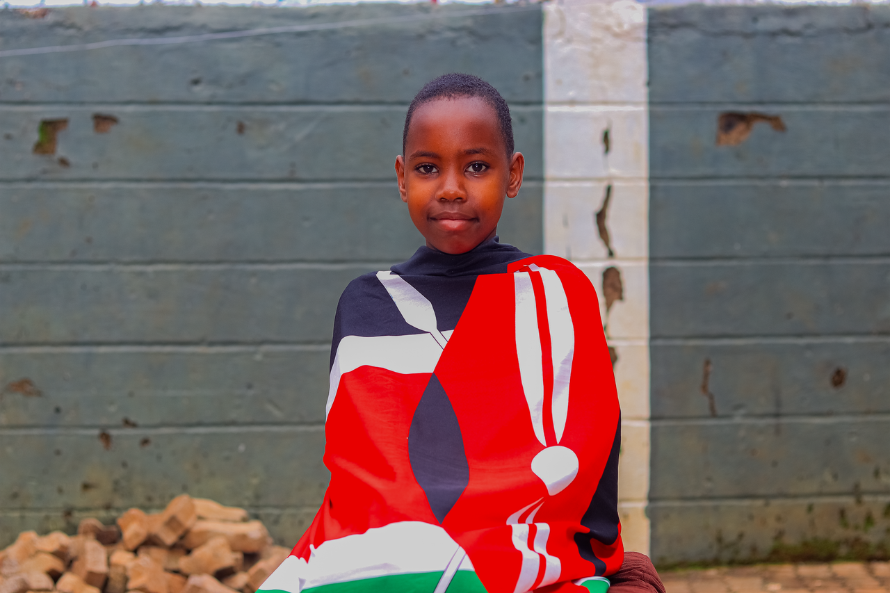 cta-02 A young Kenyan girl proudly wrapped in the national flag, showcasing cultural pride outdoors.