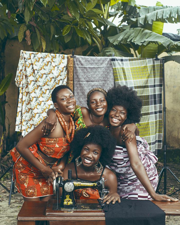 portfolio-01 Group of happy African women in colorful fabrics posing with a sewing machine outside.